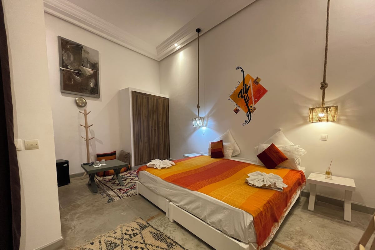 Quarto de hotel moderno com uma cama grande, uma escrivaninha, um guarda-roupa e um candeeiro suspenso.