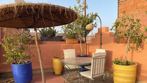An outdoor patio with a round table and chairs, surrounded by potted plants and a hanging basket.