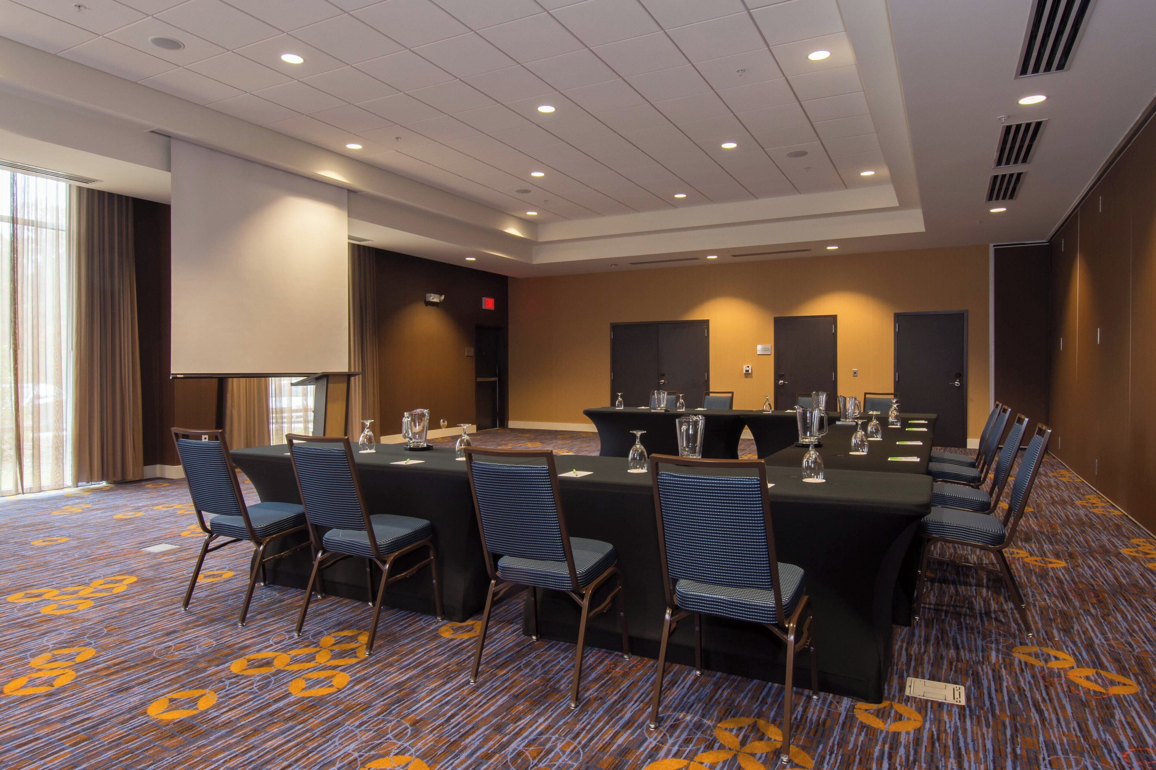 A conference room with a large table, chairs, a projector screen, and a carpeted floor.