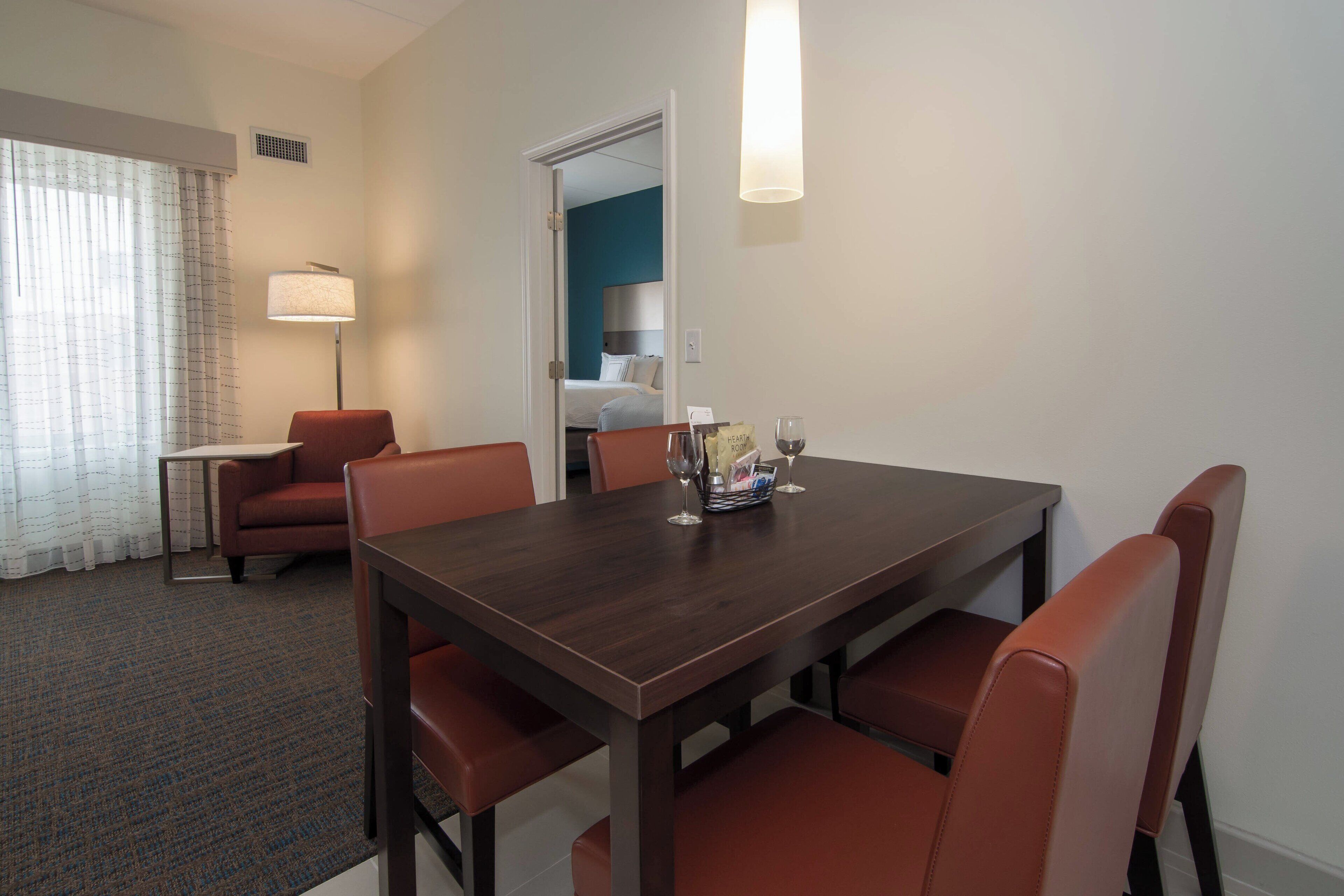 Une chambre d’hôtel comprenant une table à manger, quatre chaises, une lampe et un lit situé dans la pièce adjacente.