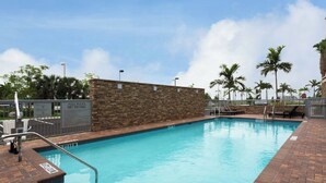 A swimming pool with a stone wall, a sign indicating pool rules, and palm trees in the background.
