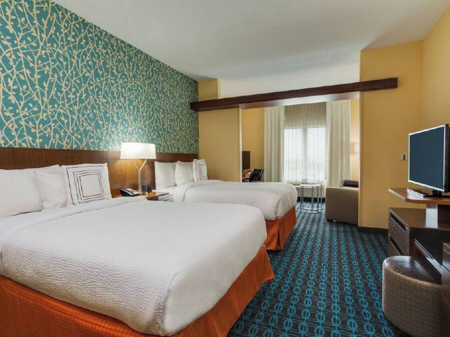 Quarto de hotel com duas camas, televisão, escrivaninha e uma cadeira.