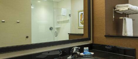 Un baño moderno con un espejo grande, una encimera negra, un lavabo blanco y un box de ducha de vidrio.