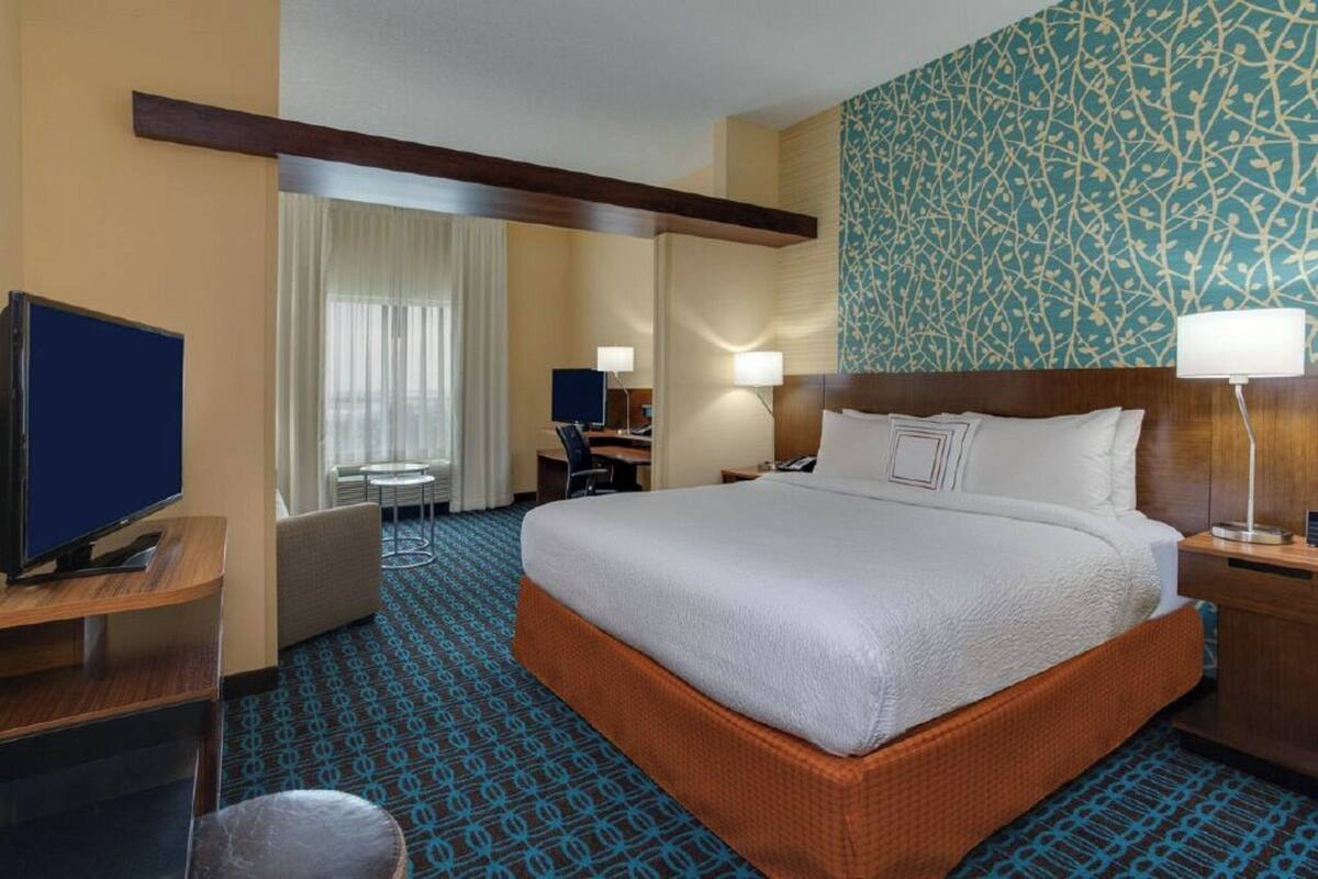 Une chambre d’hôtel avec un grand lit, un bureau avec un ordinateur, une télévision et une moquette à motifs.