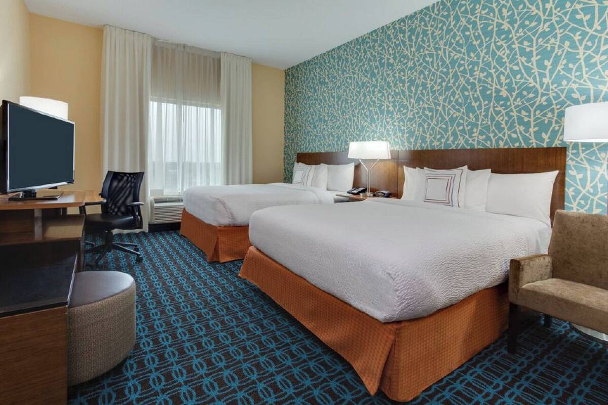 Une chambre d’hôtel avec deux lits, un bureau avec un ordinateur, une télévision et une moquette à motifs.