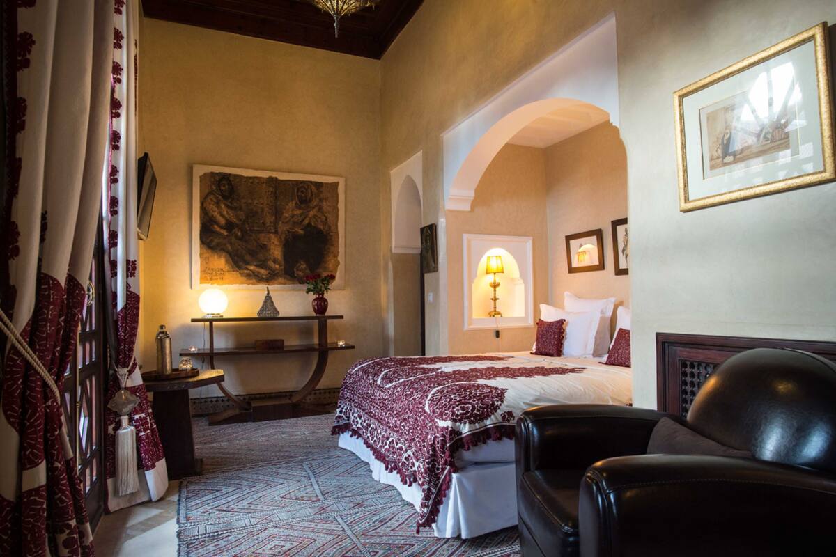 Una habitación de hotel con una cama, una silla, una lámpara y un cuadro en la pared.