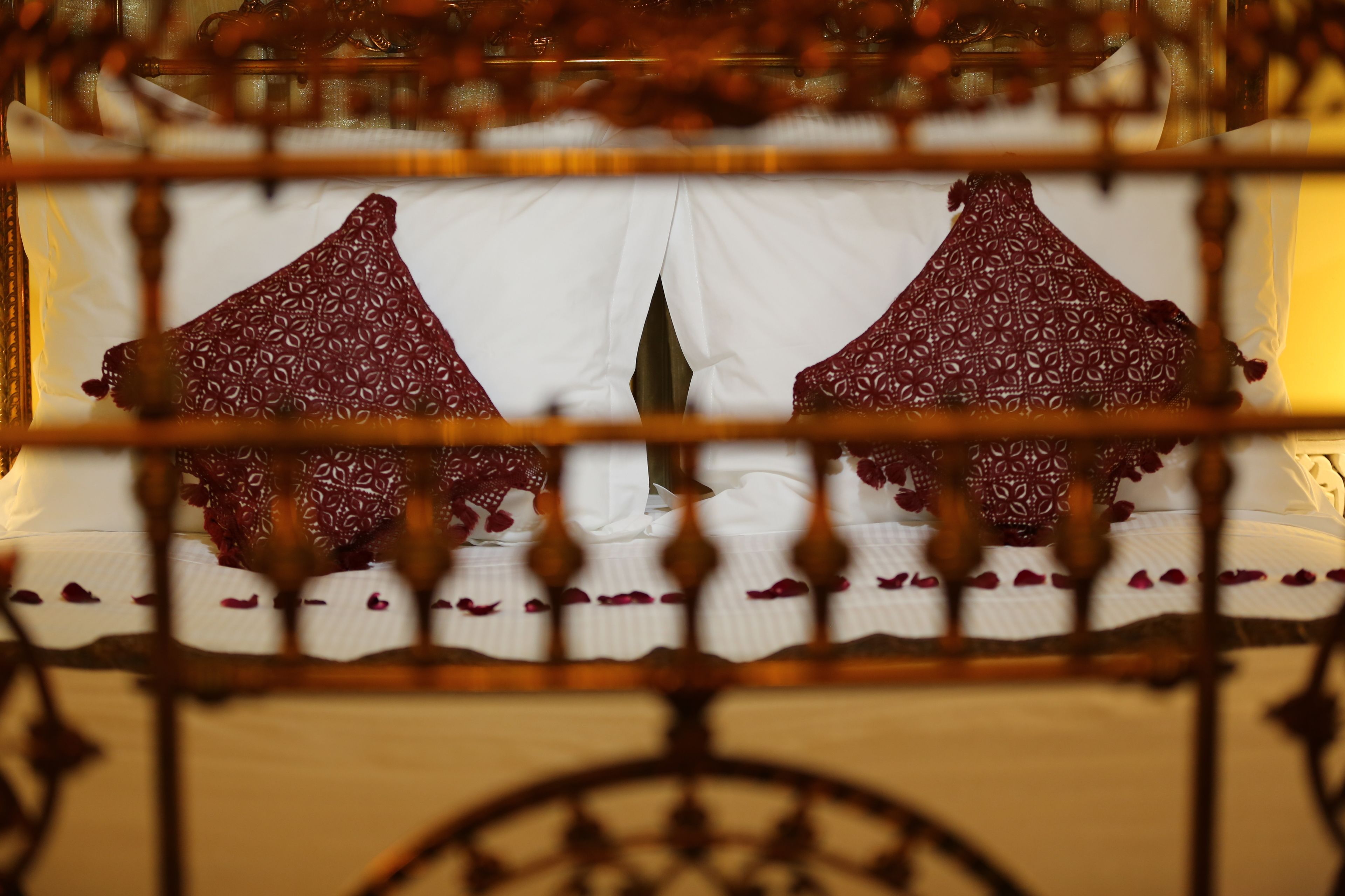 A bed with white linens and red patterned pillows, framed by a decorative wooden headboard.