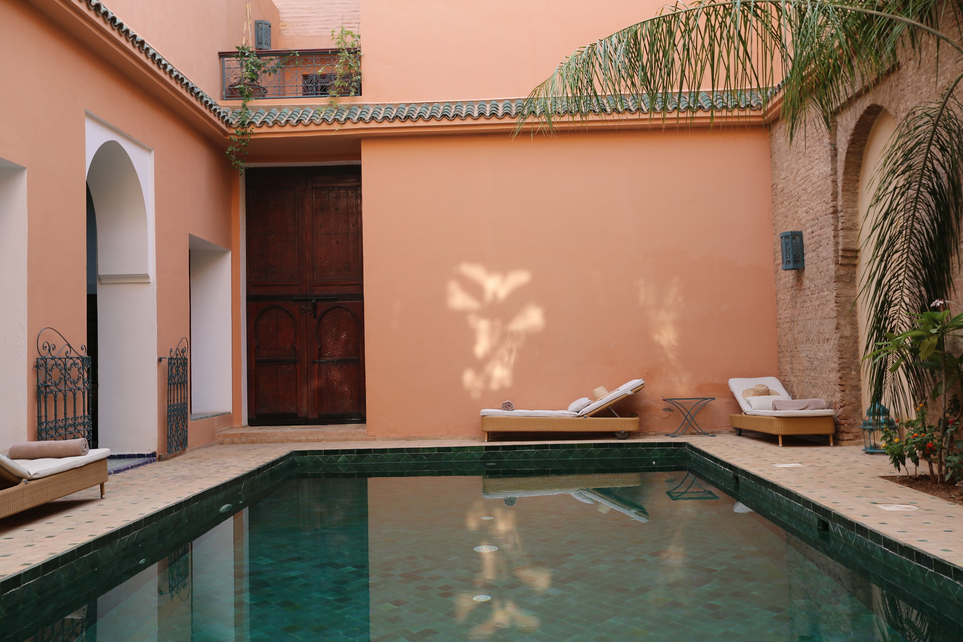 Zona de piscina con sillones de descanso, una puerta de madera y un muro con azulejos.