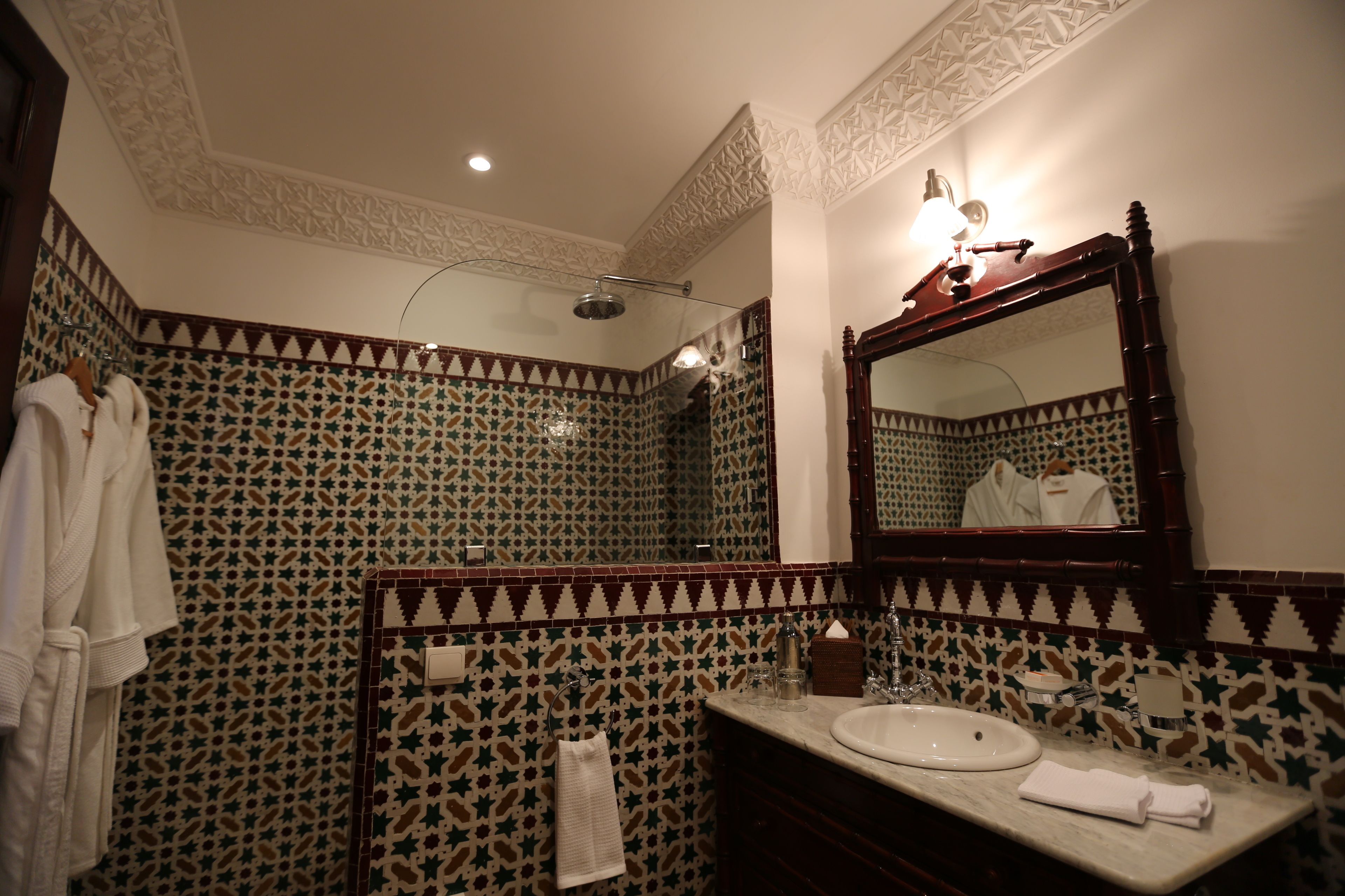 A bathroom with a patterned tile wall, a wooden vanity with a sink, and a large mirror.