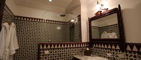 Un baño con pared de azulejos estampados, tocador de madera con lavamanos y un espejo grande.