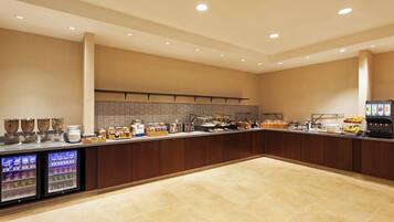 A spacious, well-lit breakfast area with a long counter, refrigerated beverage dispensers, and a variety of food and drink options.