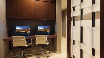 A modern office space with two desks, each with a computer monitor, office chair, and wooden cabinets above.