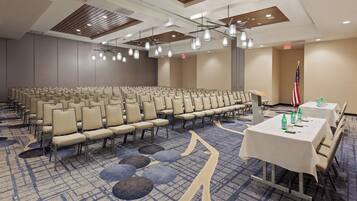 A conference room with rows of chairs, tables with water bottles, and an American flag.
