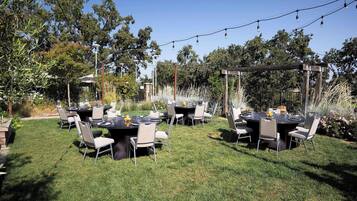 An outdoor dining area with tables and chairs, surrounded by greenery and trees.