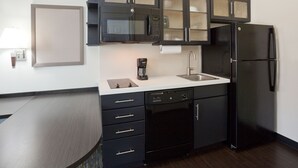 A modern kitchen with black cabinetry, a stainless steel refrigerator, a coffee maker, and a dishwasher.