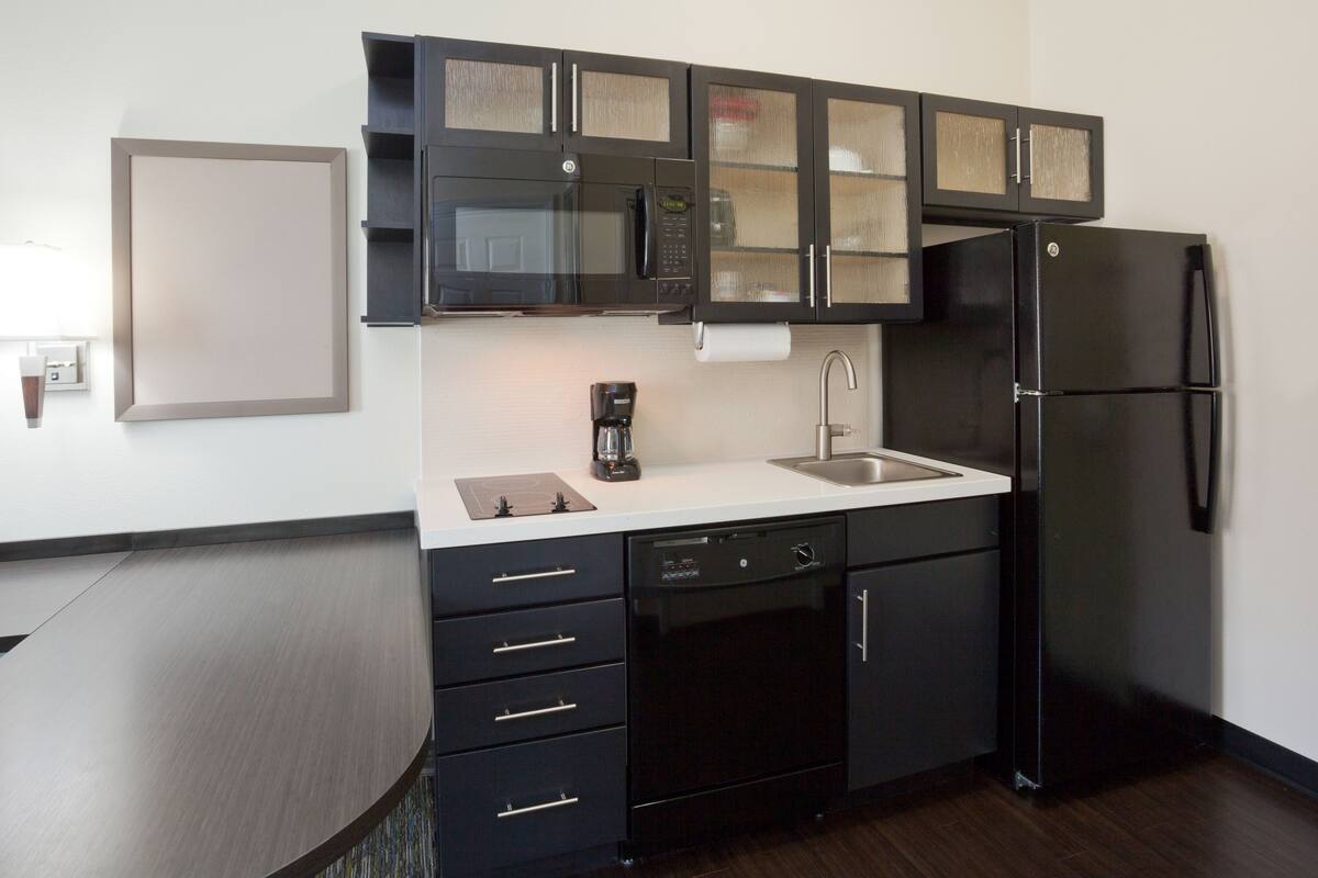 A modern kitchen with black cabinetry, a stainless steel refrigerator, a coffee maker, and a dishwasher.