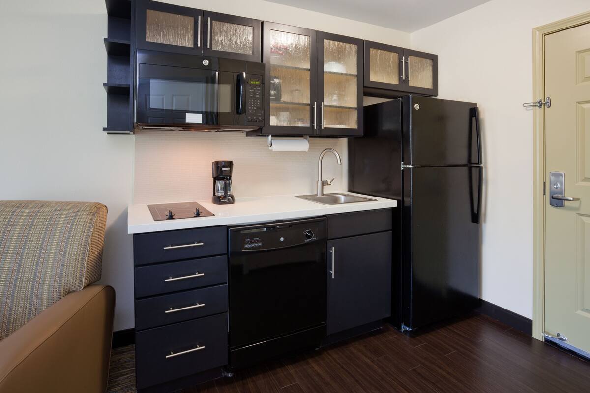 A compact kitchen with dark cabinetry, a built-in microwave, a refrigerator, and a dishwasher.