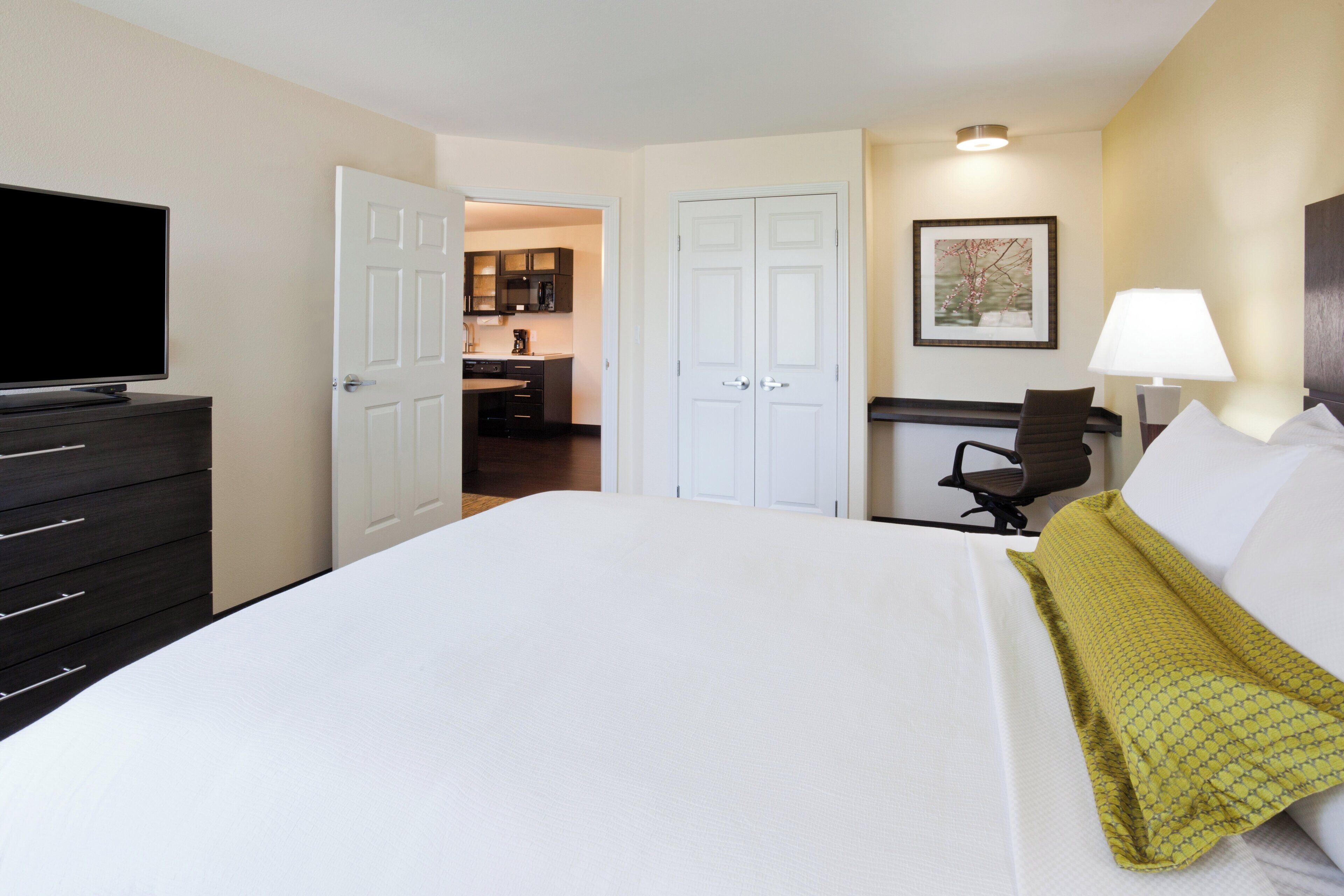 Una habitación de hotel con cama, escritorio, silla, televisor y una zona de cocina.