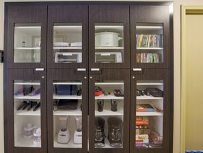 Armário de cozinha com vários compartimentos contendo eletrodomésticos, utensílios de cozinha e uma pequena seleção de livros.