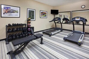 Une salle de sport équipée de tapis de course, d’un banc et d’un porte-haltères.