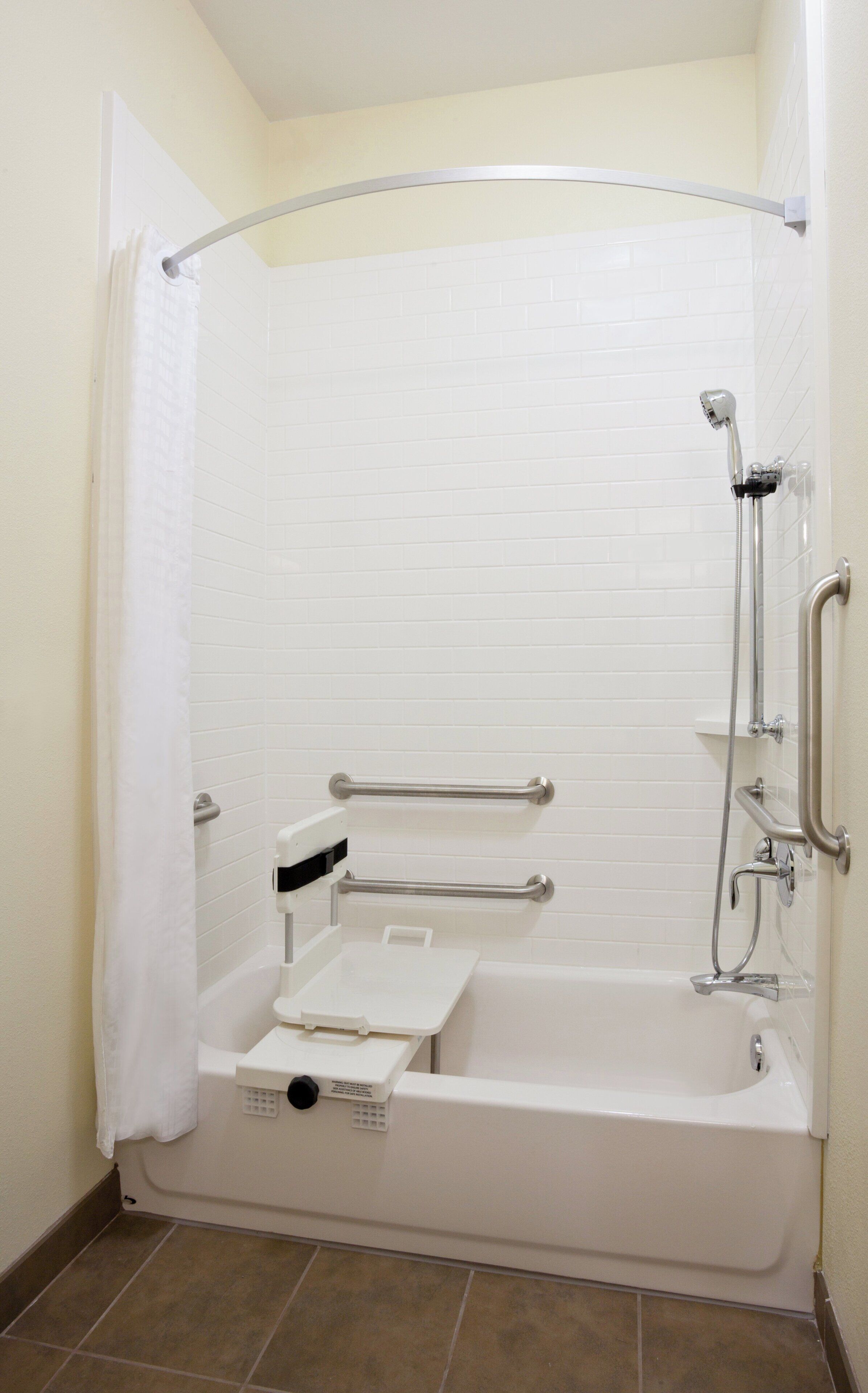 A standard shower stall with a grab bar, a handheld showerhead, and a seat.