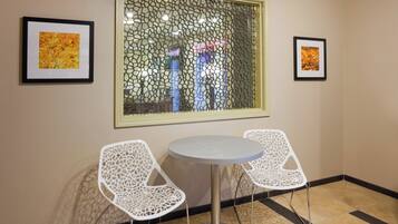 A room with a round table and two white chairs with intricate designs, a window with a decorative screen, and two framed pictures on the wall.