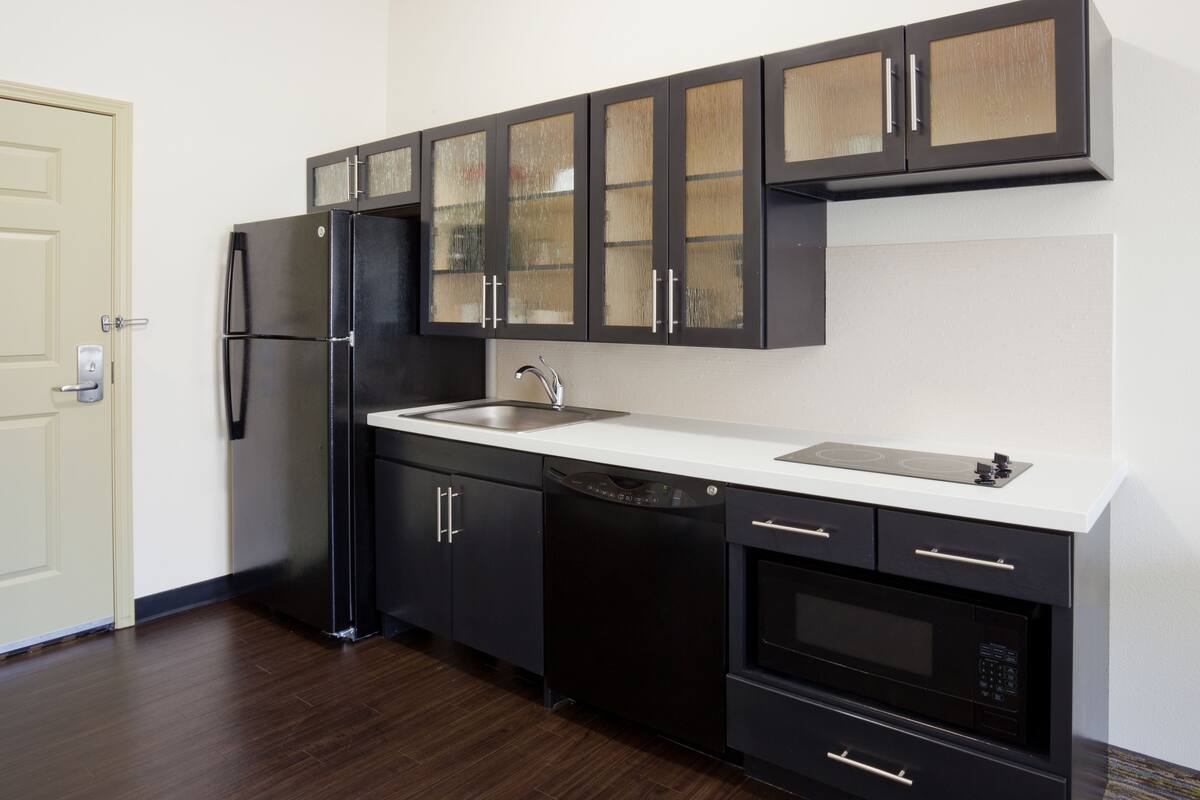 A modern kitchen with black cabinets, a stainless steel refrigerator, a dishwasher, and a built-in oven.