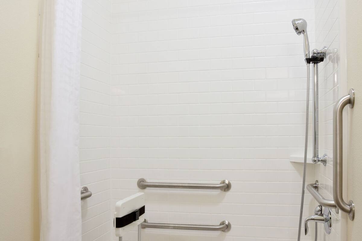 A walk-in shower with a grab bar, a handheld showerhead, and a seat.