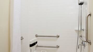 Eine bodenebene Dusche mit Haltegriff, Handbrause und Sitzgelegenheit.