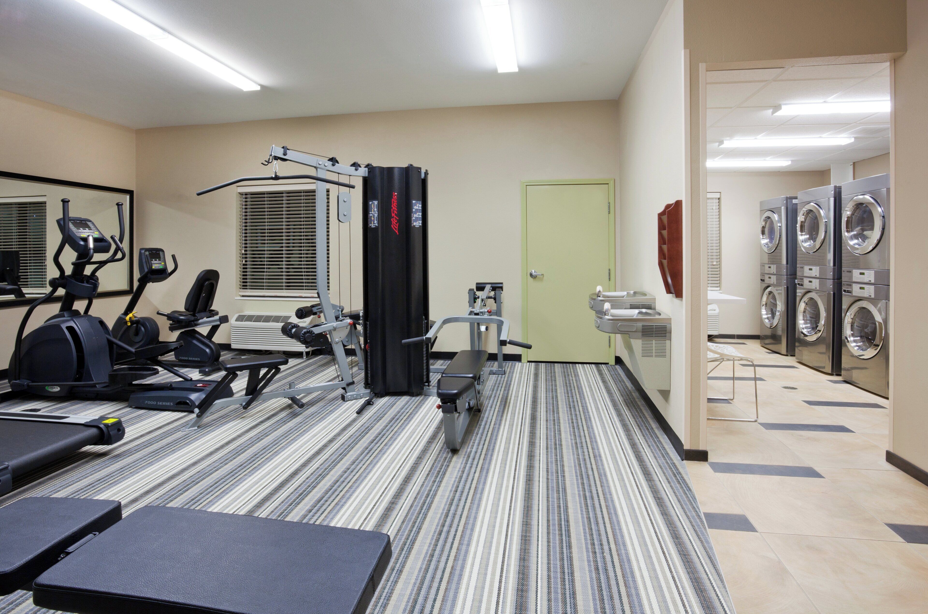 Un gimnasio con equipo de ejercicio, un espejo y zona de lavandería con lavadoras y secadoras.