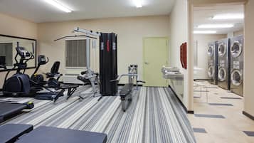 Un gimnasio con equipo de ejercicio, un espejo y zona de lavandería con lavadoras y secadoras.