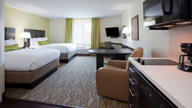 A hotel room with two beds, a dining table, a TV, and a kitchenette.