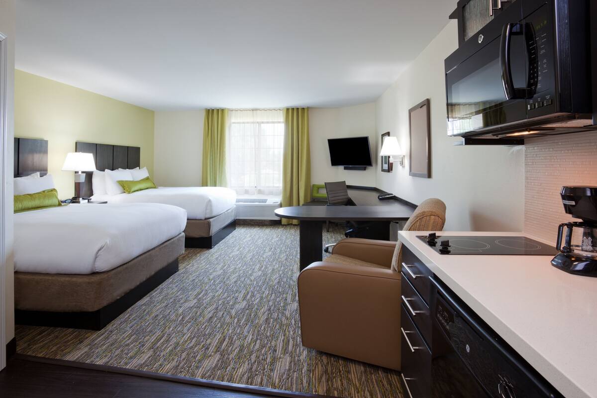 A hotel room with two beds, a dining table, a TV, and a kitchenette.