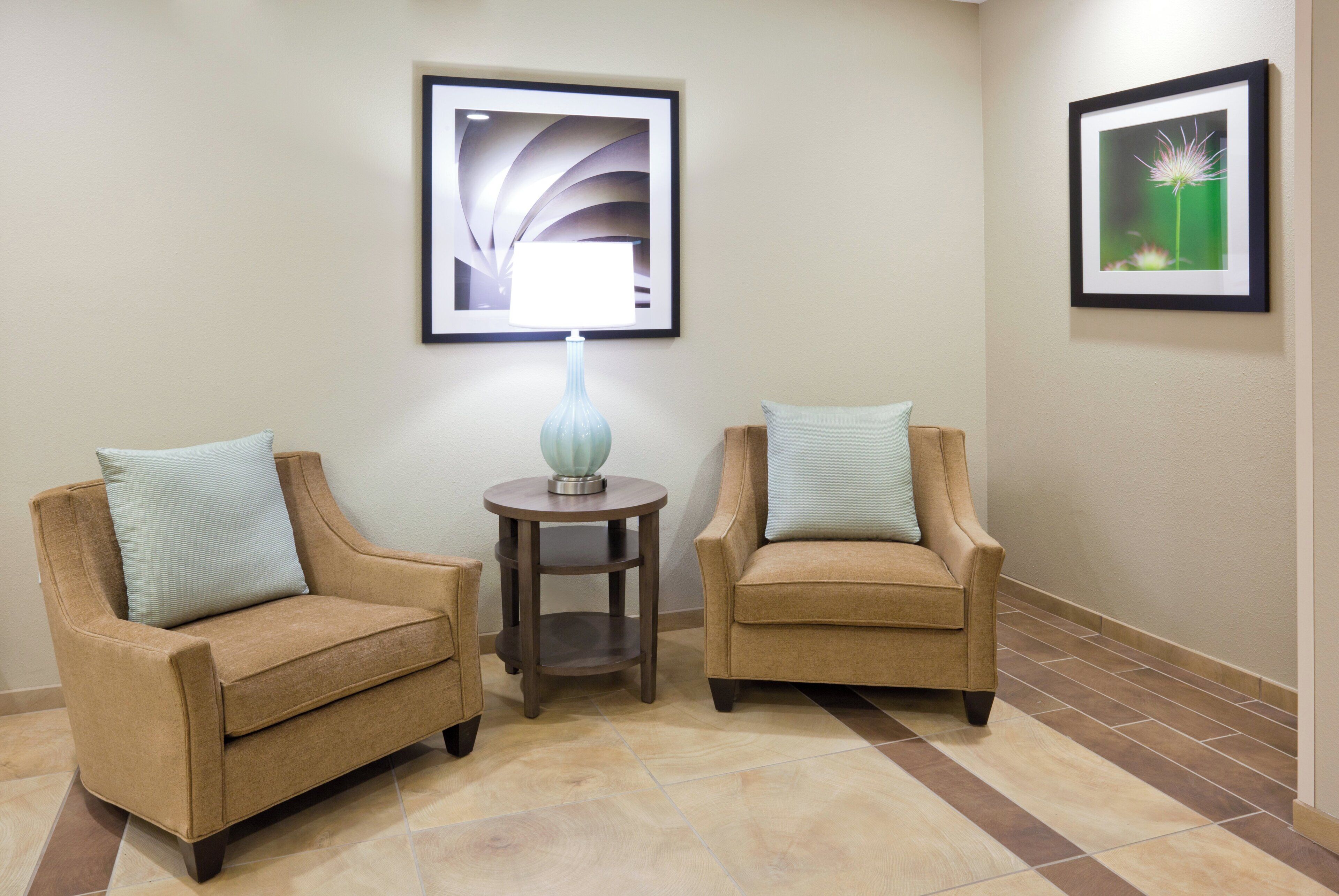 Two armchairs with light blue cushions, a small table with a lamp, and two framed pictures on the wall.
