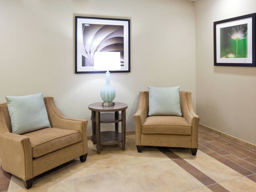 Two armchairs with light blue cushions, a small table with a lamp, and two framed pictures on the wall.
