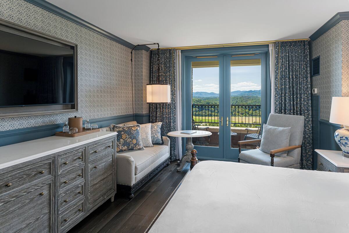 A hotel room with a bed, a sofa, a TV, a table, and a view of the outdoors.