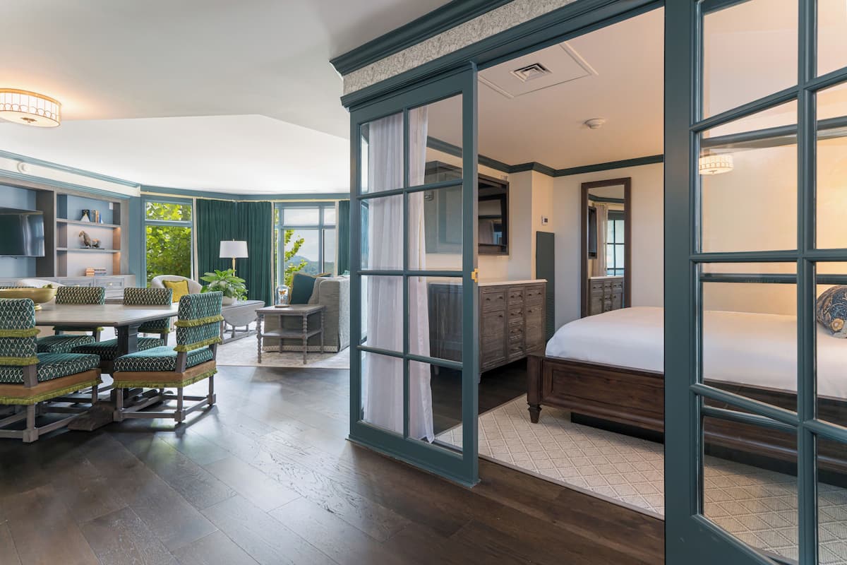 A room with a bed, a dining table with chairs, a sofa, a desk, and a window with curtains.