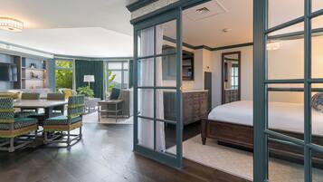 A room with a bed, a dining table with chairs, a sofa, a desk, and a window with curtains.