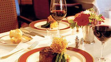 Una mesa de comedor dispuesta con platos, cubiertos, una copa de vino tinto y un centro de mesa con flores.