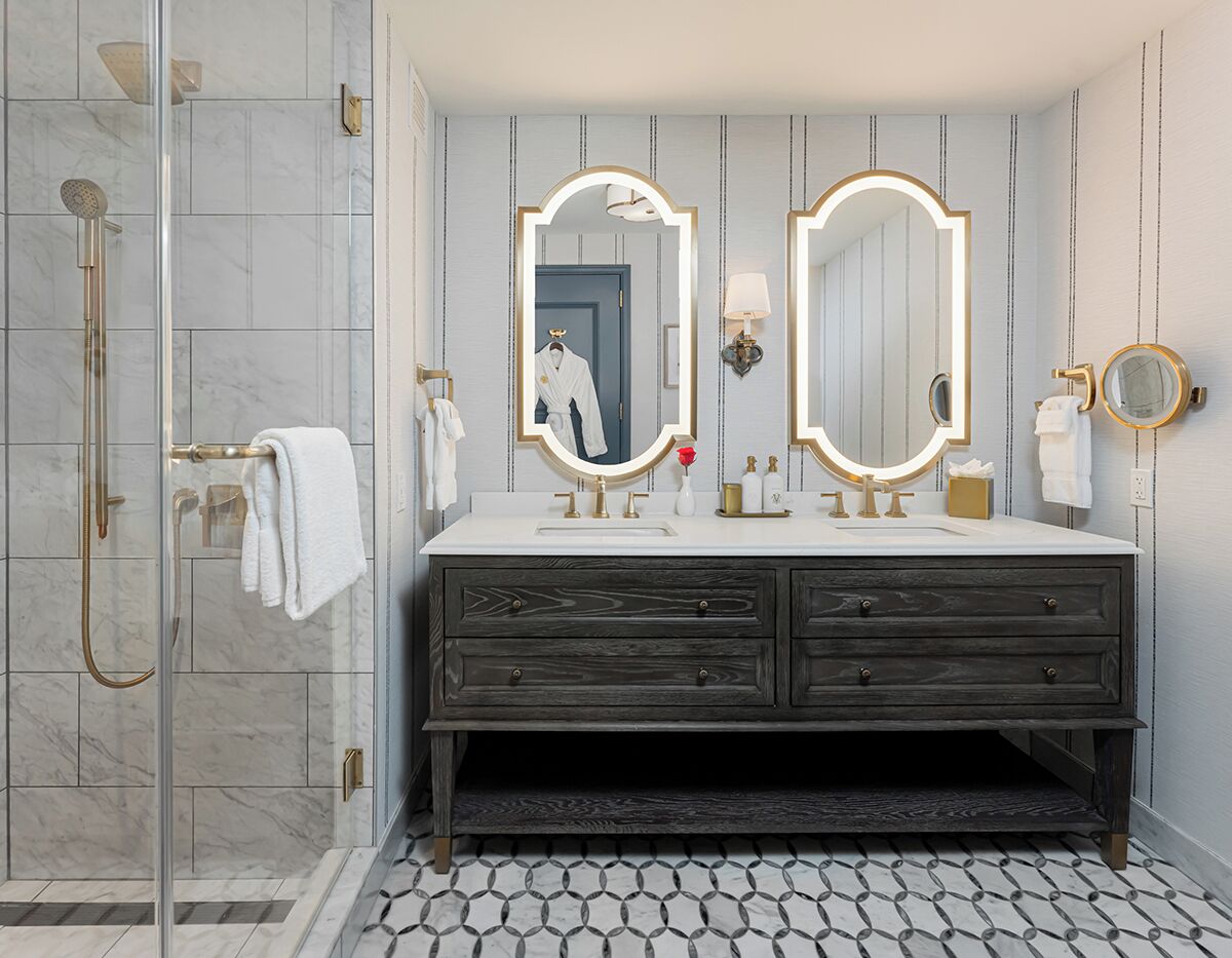 A bathroom with a glass shower enclosure, a vanity with two mirrors, and a dark wooden cabinet.