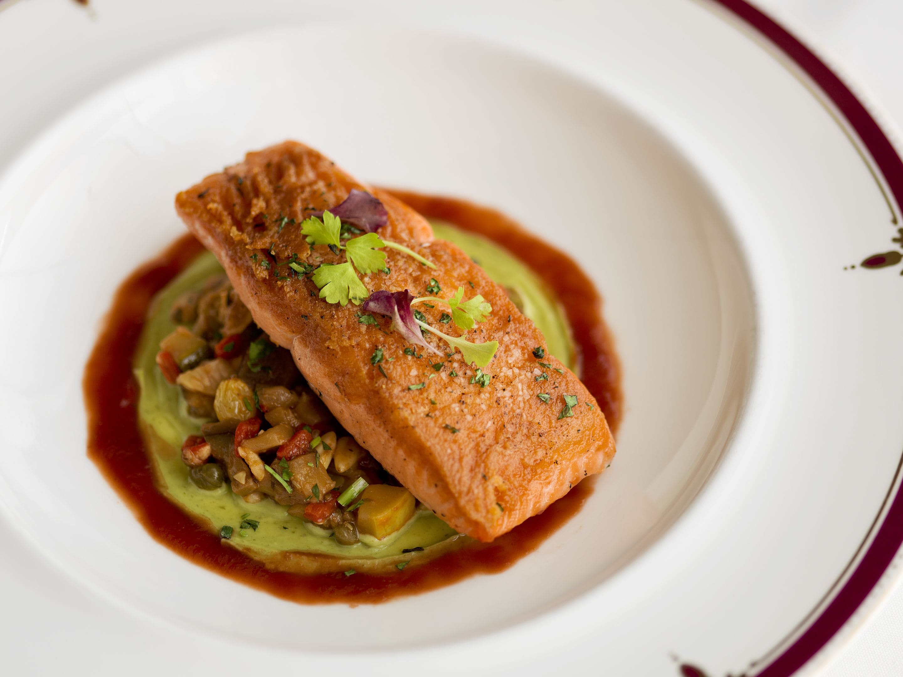 Een zalmfilet op een bord met een groene saus en groenten.