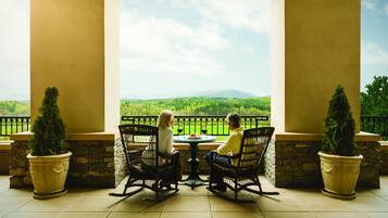 A terrace with two rocking chairs facing a scenic view of a green landscape and mountains.