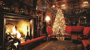 A warmly lit library with a large Christmas tree, red upholstered chairs, and a fireplace. - The Inn on Biltmore Estate (Asheville)