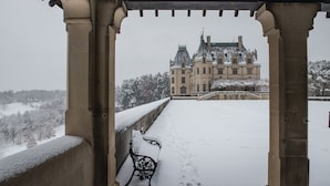 A snow-covered balcony with a bench, overlooking a historic building with a snow-covered landscape. - The Inn on Biltmore Estate (Asheville)