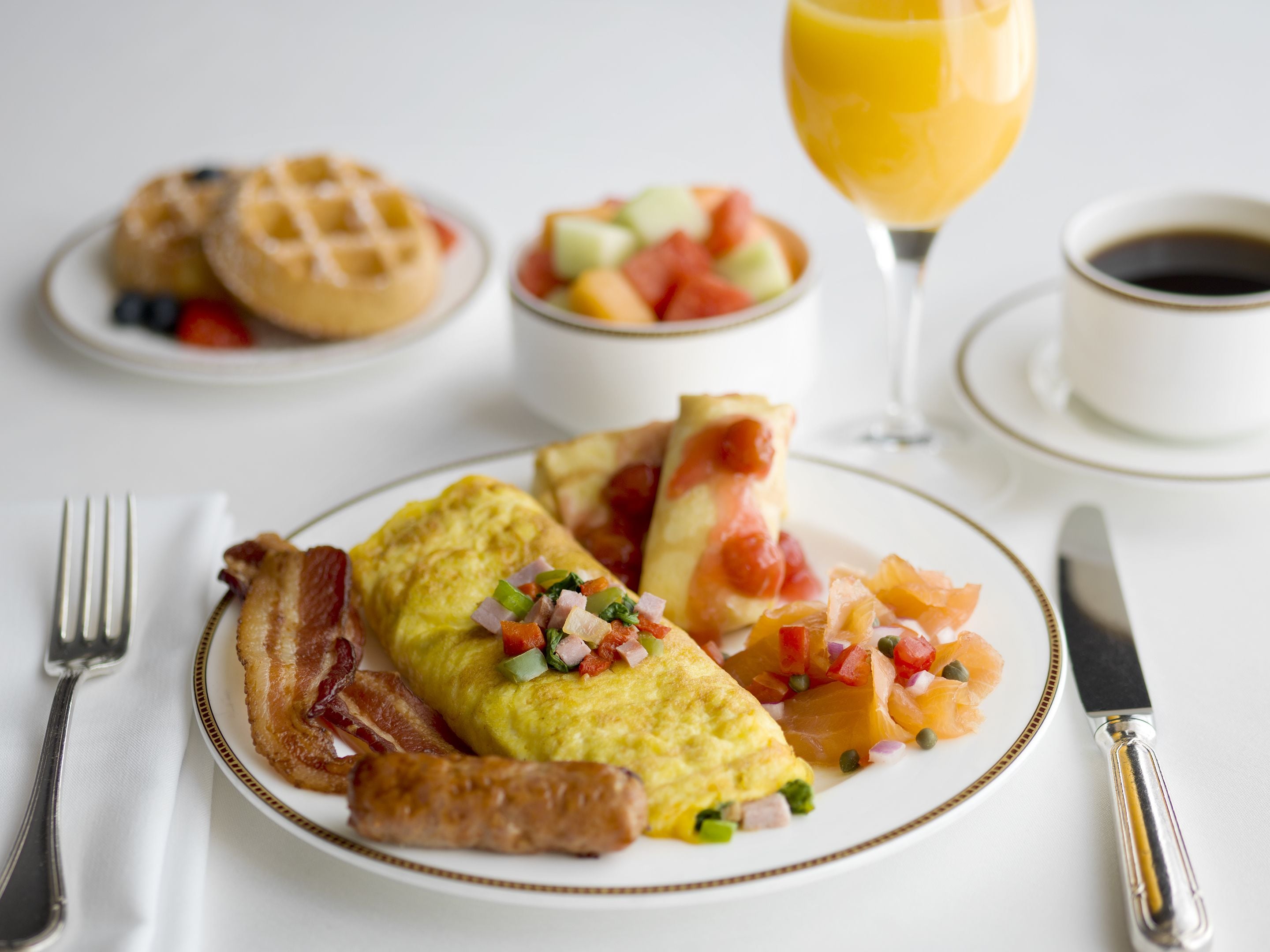 A breakfast plate with eggs, bacon, sausage, and a fruit salad.