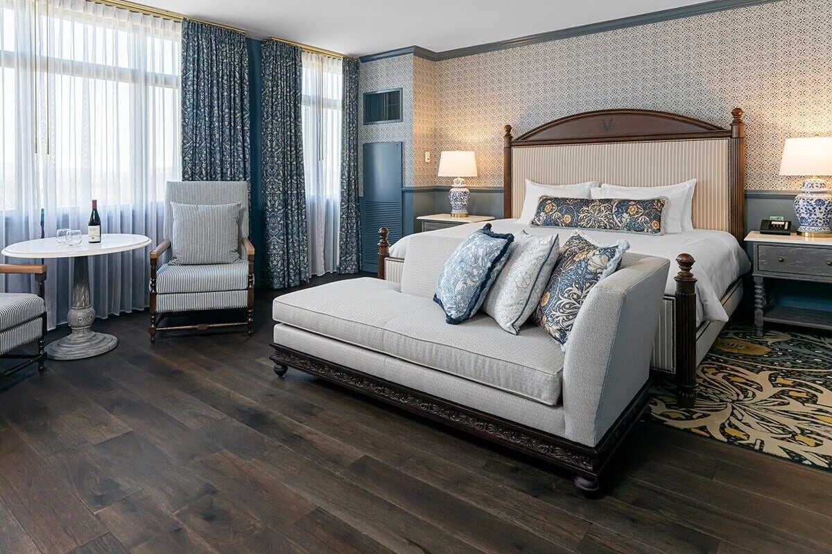 A hotel room with a bed, a sofa, a chair, a round table, and a patterned rug.