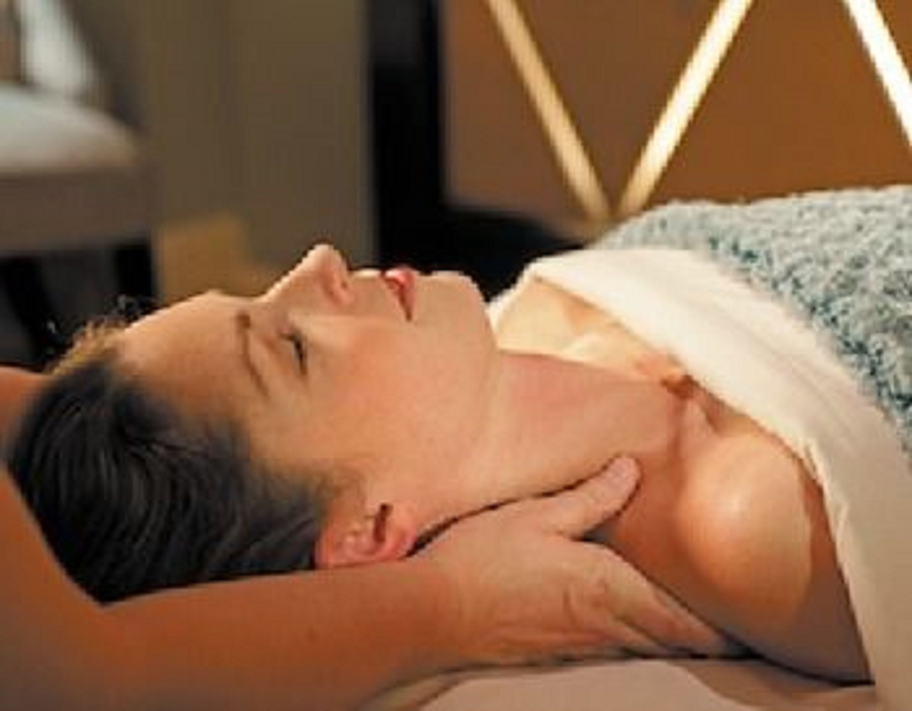 A person lying in a bed with a headboard, covered with a blanket.
