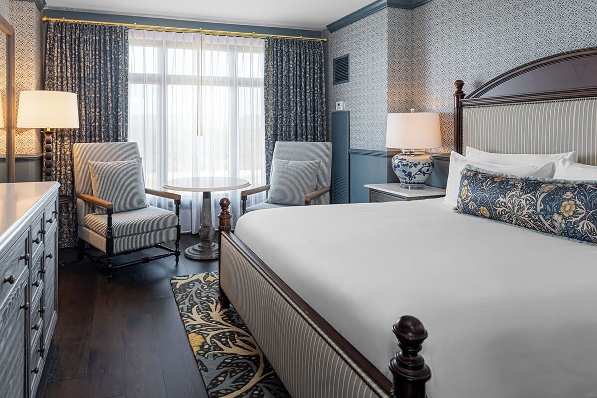 A hotel room with a large bed, two armchairs, a small table, and a nightstand with lamps.