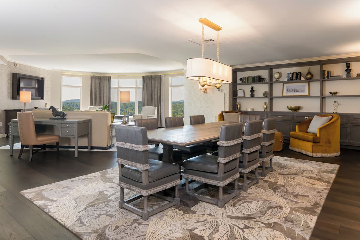 A dining area with a large table, multiple chairs, a chandelier, and a view of the outdoors.