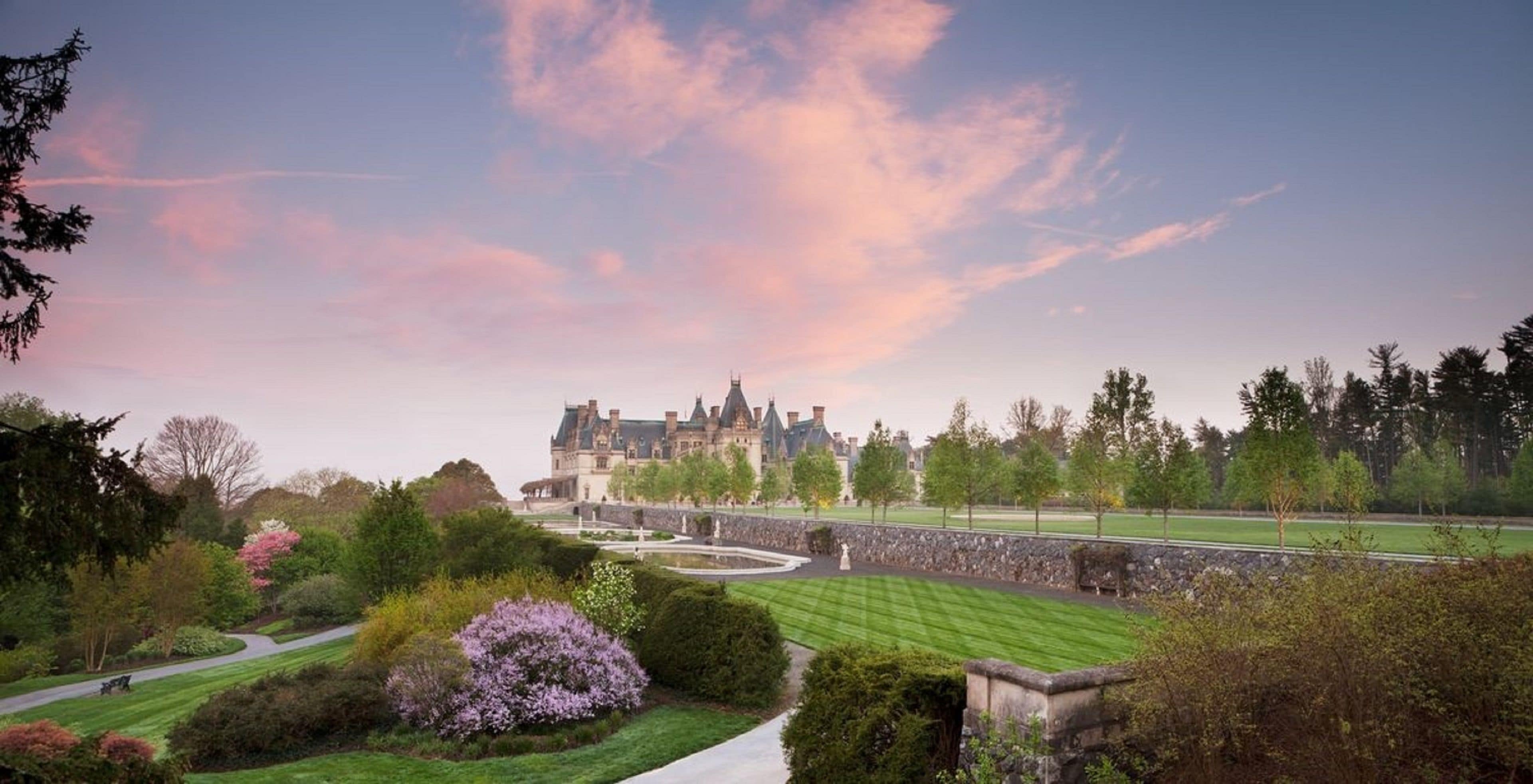A large, historic building with a well-maintained lawn and stone pathway leading to it.